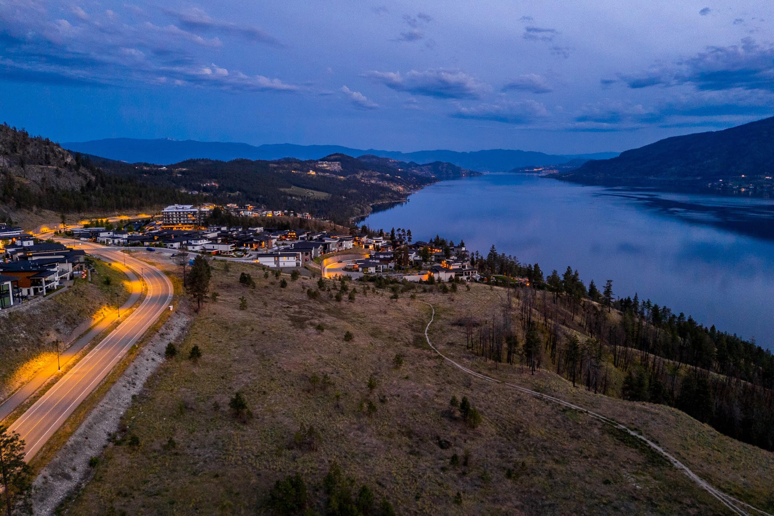 The road into Lakestone lit at dusk, its houses on the hillside and Okanagan Lake beyond
