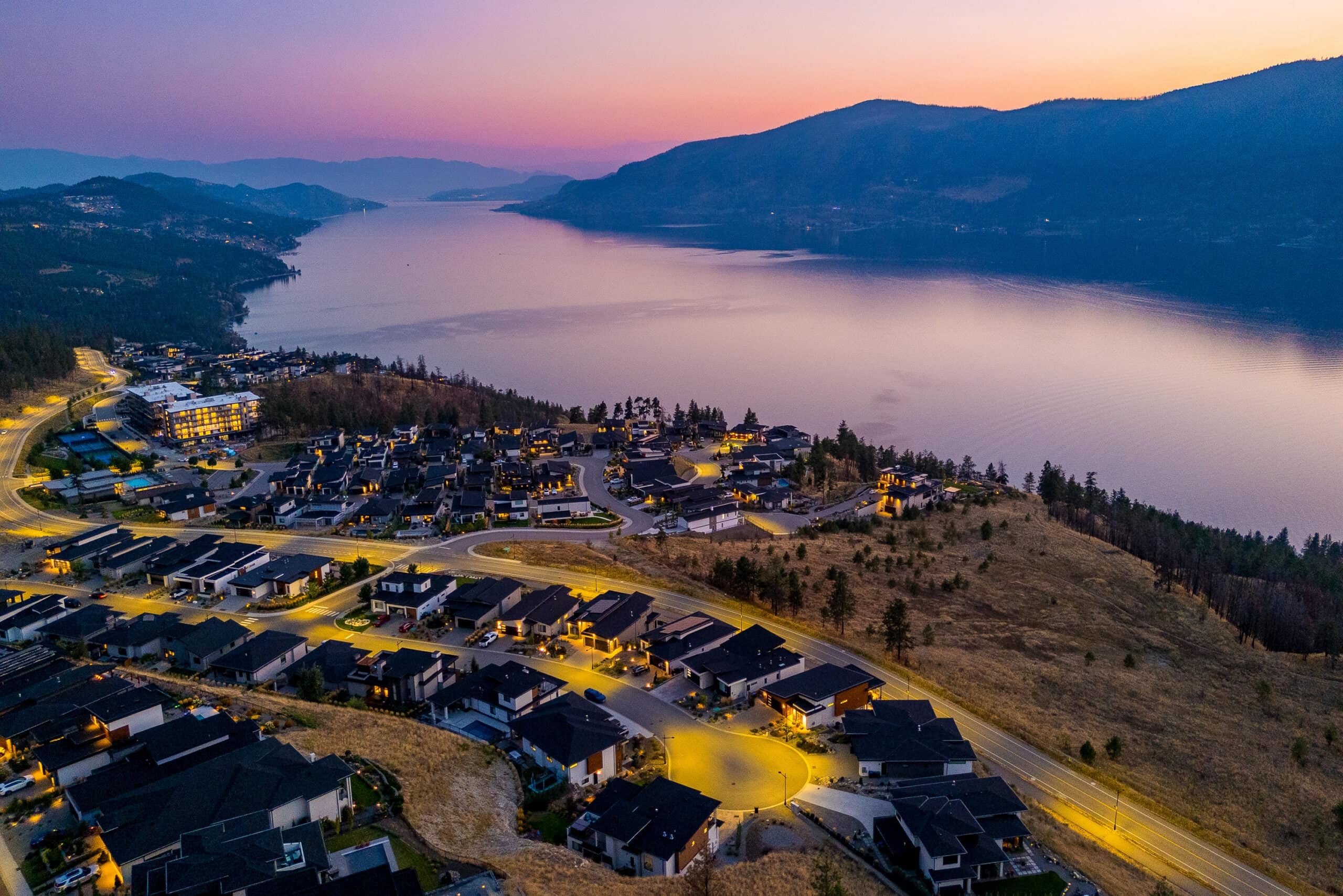 Lakestone's lit streets at dusk above Okanagan Lake, looking south down the lake, with the dry slope of Tyndall Bench at the right